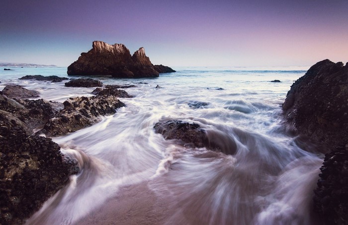 Ocean waves crashing on rocky shore at sunset