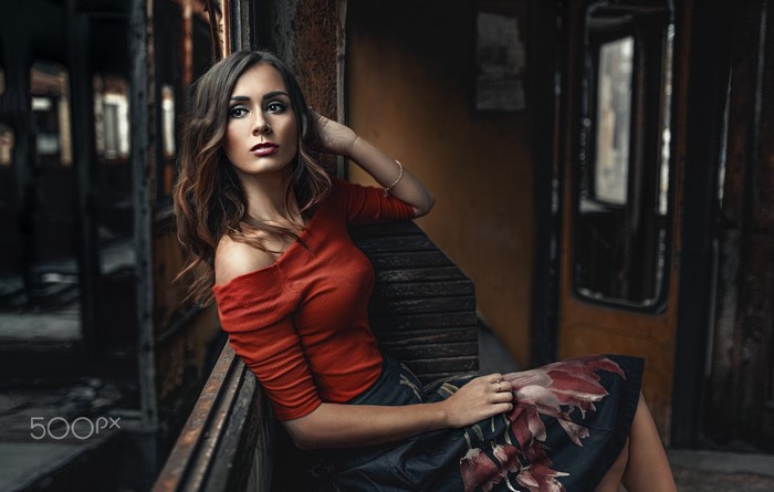 Woman in red top and floral skirt sitting in train