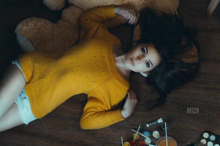 Woman in yellow sweater lying on floor with teddy bear