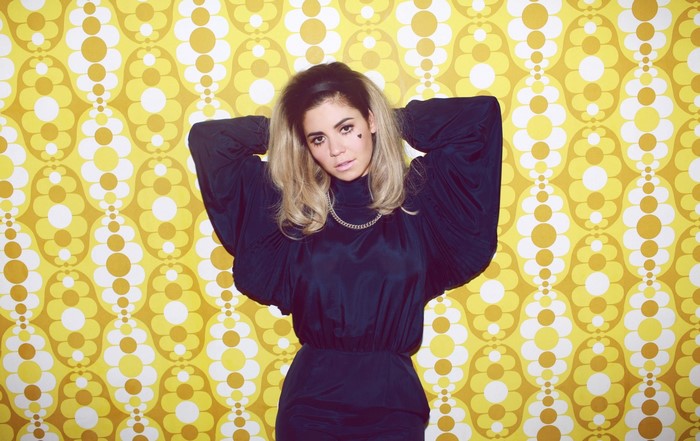 Marina Diamandis in a blue dress with a floral yellow background