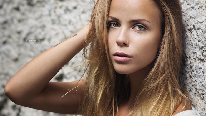 Woman with blonde hair leaning against a rock wall