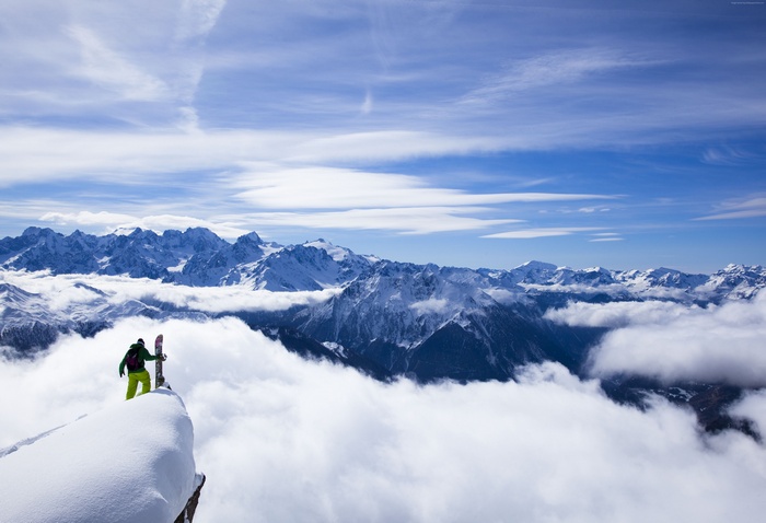 Snowboarder on a snowy mountain peak above clouds