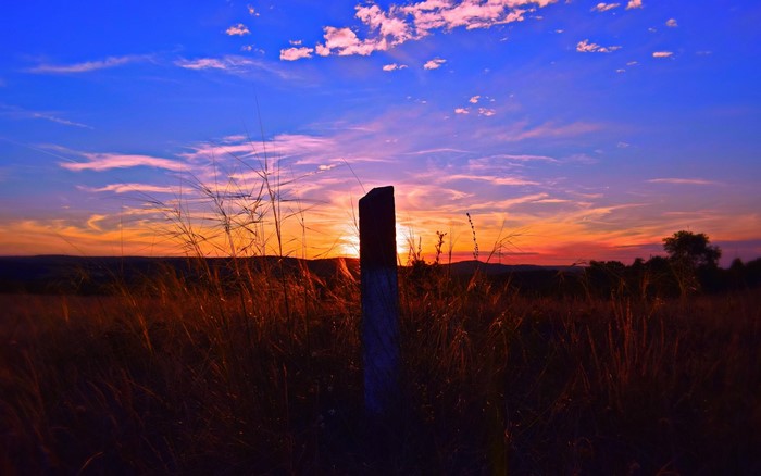 Sunset over a field with a fence post