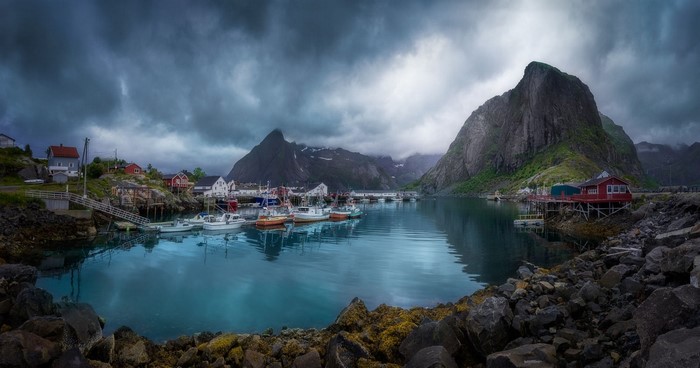 Fishing village with boats in a Norwegian fjord under overcast sky