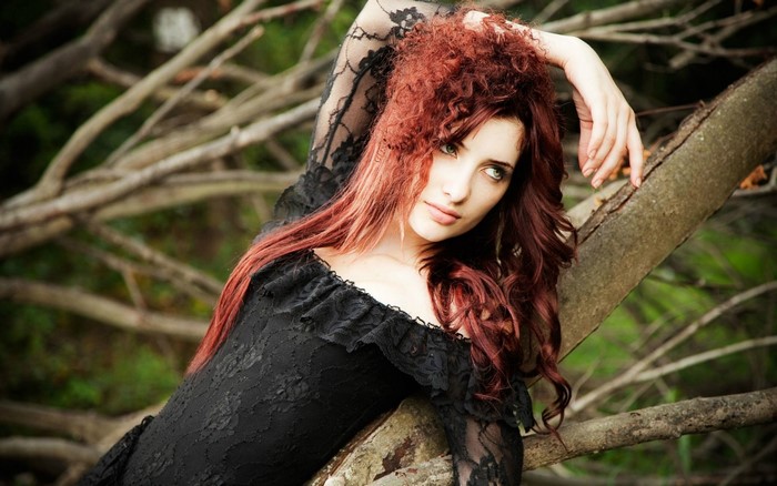 Redhead woman in black lace dress sitting on a tree branch
