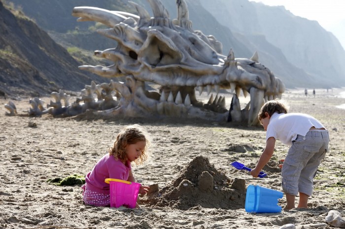 Children playing on a beach with a dragon skeleton sculpture