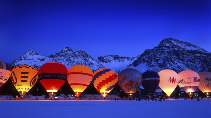 Hot air balloons at night with snowy mountains