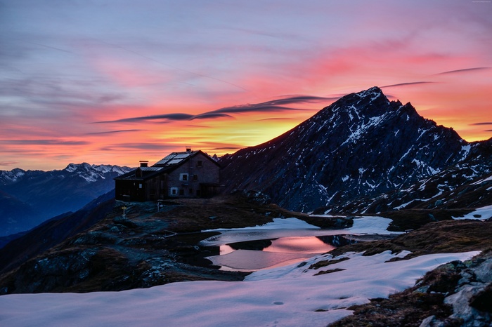 Mountain hut at sunrise with snow and lake