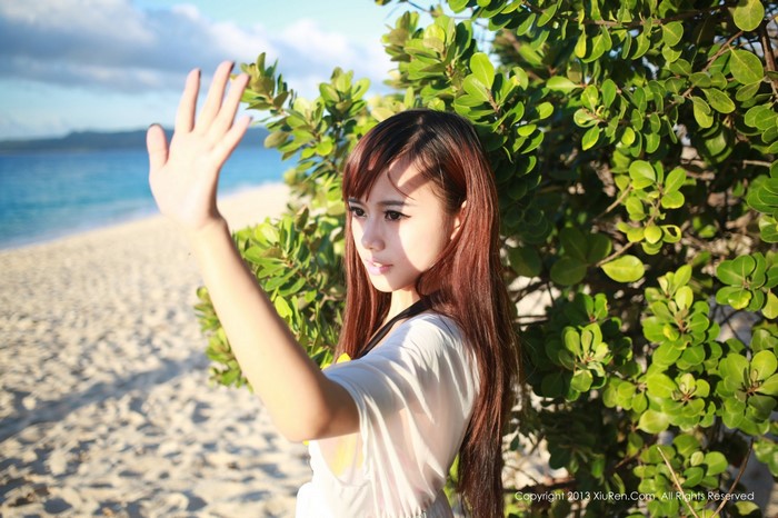Asian woman waving hand on beach near green tree