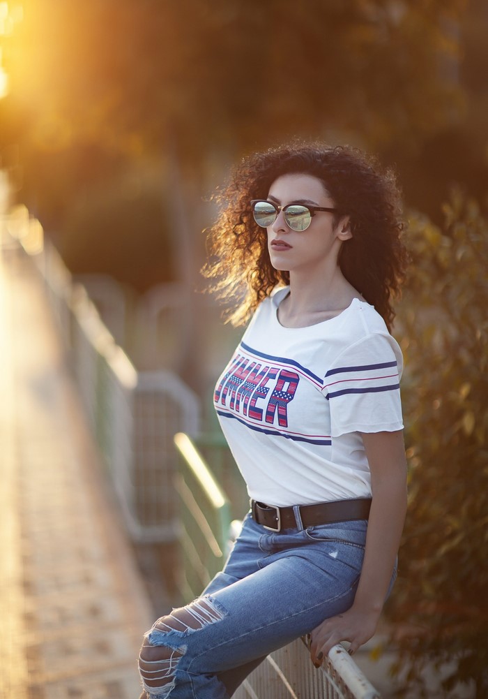 Woman with curly hair wearing sunglasses and a t-shirt