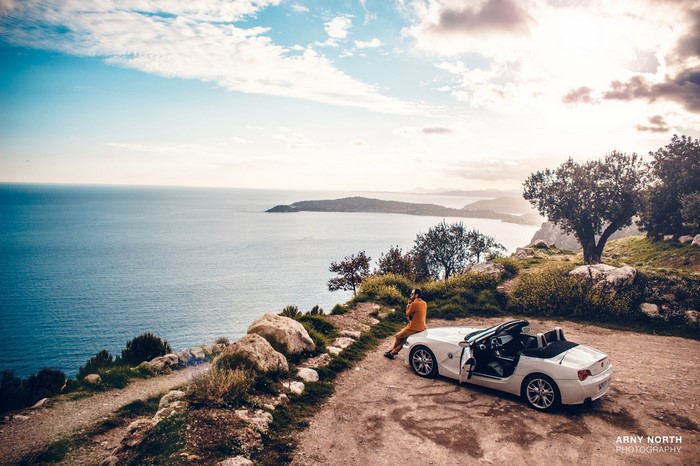 Man and white BMW Z4 on cliff overlooking sea at sunset