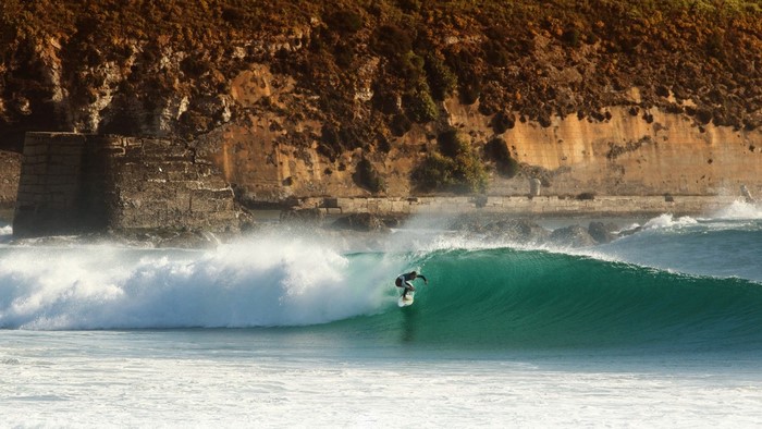 Surfer riding a wave near a rocky cliff