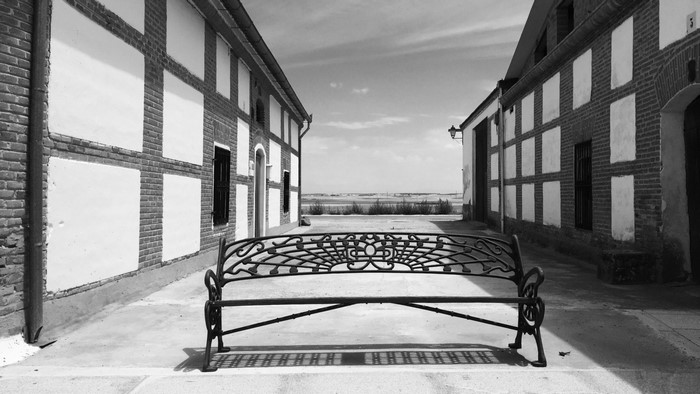 Black and white image of a village street with a bench