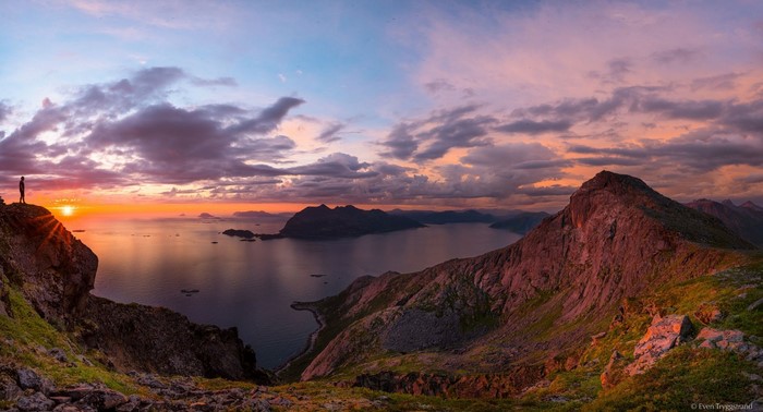 Man on cliff overlooking ocean at sunset
