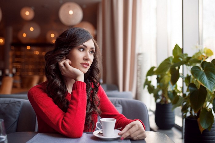 Woman in red sweater sitting at a table with a cup
