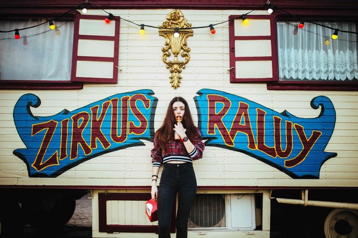 Woman in plaid shirt in front of Zirkus Ralu circus trailer