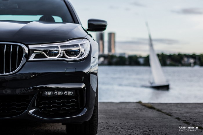 Black BMW 7 Series Sedan by a lake with a sailboat