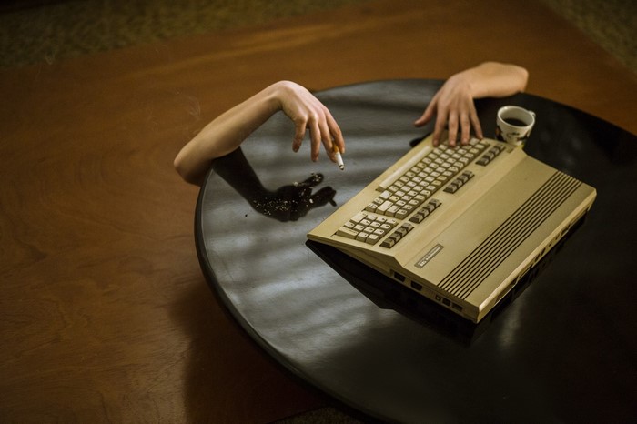 Arms reaching from a table with a computer and cigarette