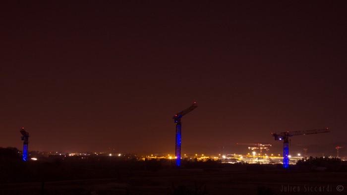 Cityscape with illuminated construction cranes at night
