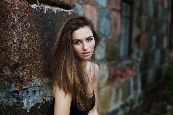 Woman with long brown hair leaning against a stone wall