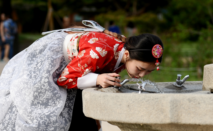 Woman in Hanbok drinking water from a fountain