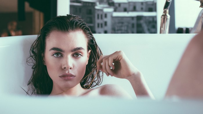 Woman with wet hair in a bathtub holding a necklace