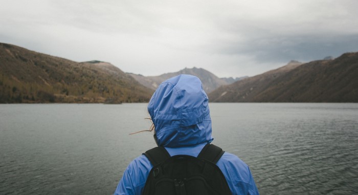 Person in blue jacket looking at a lake and mountains