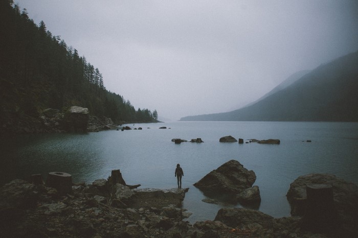 Person standing on rocks by a misty lake with mountains