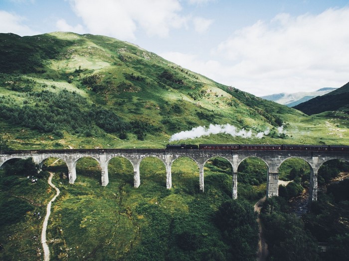 Steam train crossing a viaduct in a green mountainous landscape