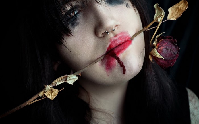 Woman with dried rose through mouth and nose ring