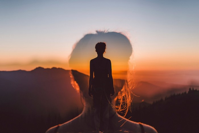 Double exposure of a woman against a sunset mountain landscape