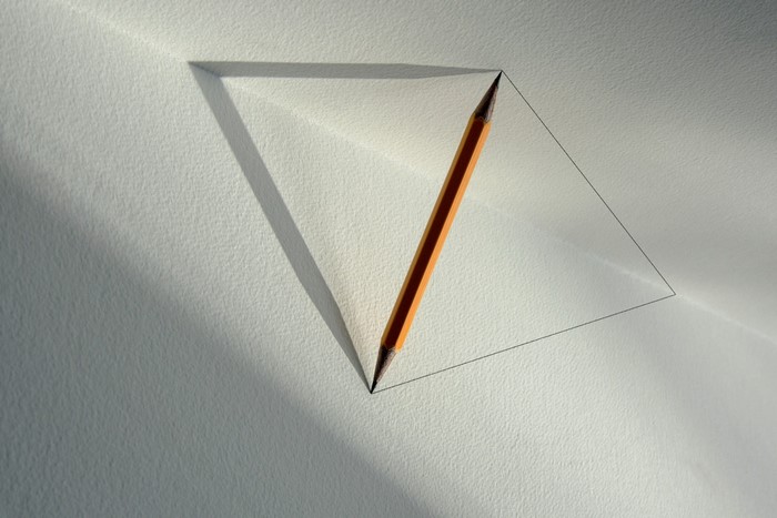 Pencil drawing a triangle on textured paper with shadows