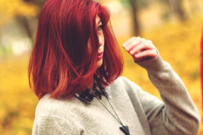 Woman with red hair in a grey sweater outdoors