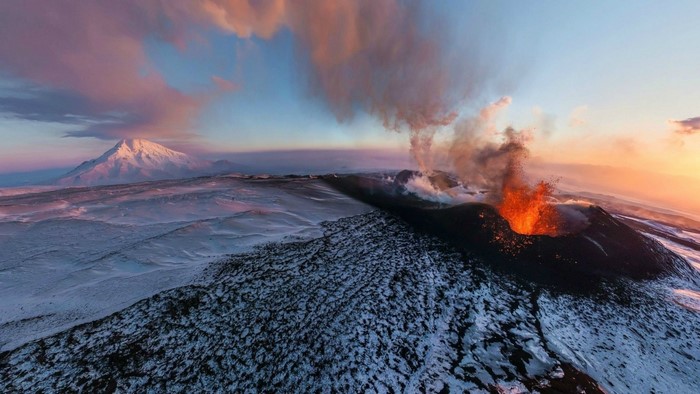 Volcano erupting at sunrise with snow-covered landscape