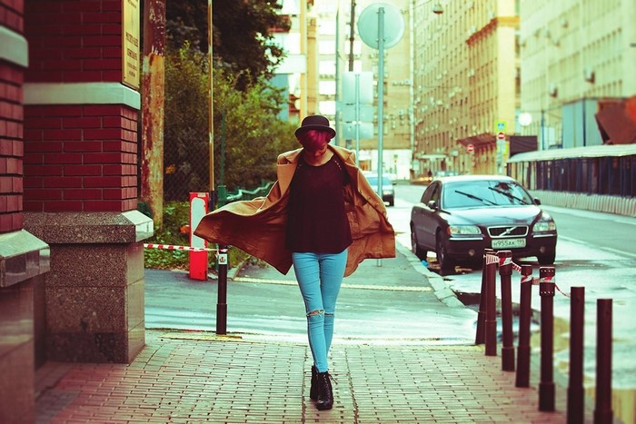 Woman in trench coat and torn jeans walking on sidewalk