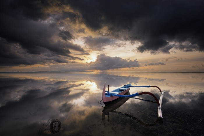 Boat on calm sea during sunset with dramatic clouds