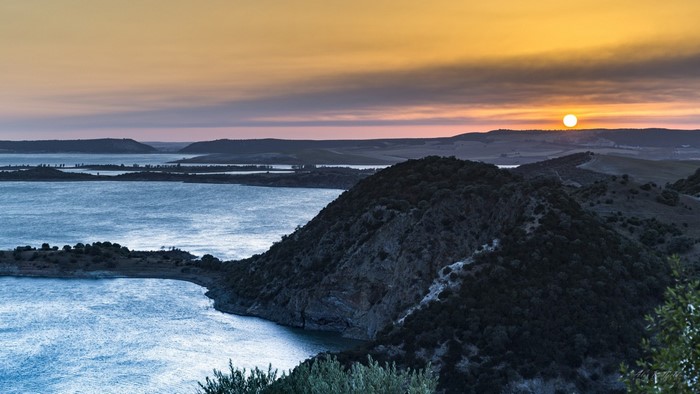 Sunset over a vast body of water with rolling hills