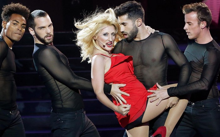 Singer in red dress with male dancers on stage