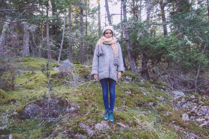 Woman in a forest wearing a sweater and scarf