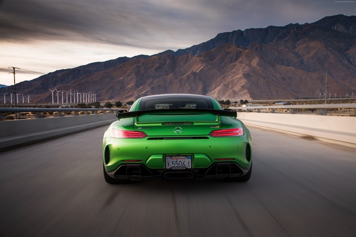 Green Mercedes-AMG GT R driving on a highway with mountains and wind turbines in the background