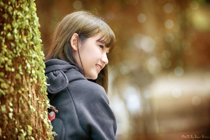 Young Asian woman in a black hoodie near a tree