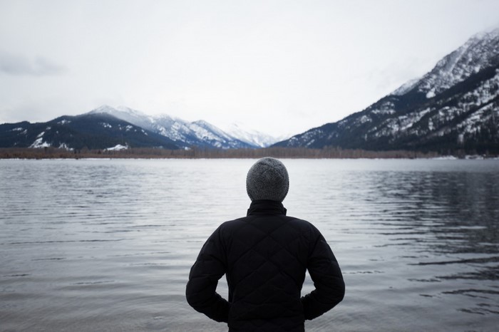 Person in a hat and jacket by a lake with mountains
