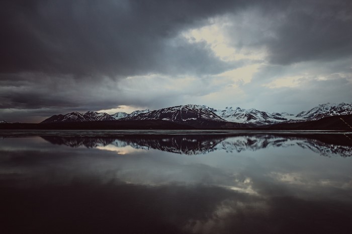 Snow-capped mountains reflected in a dark lake under stormy clouds