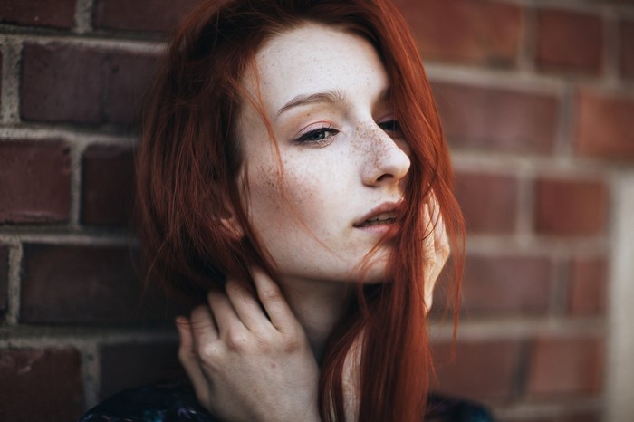 Redhead woman with freckles posing against brick wall