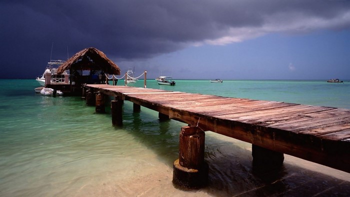 Wooden pier with thatched hut and boats in the Caribbean sea