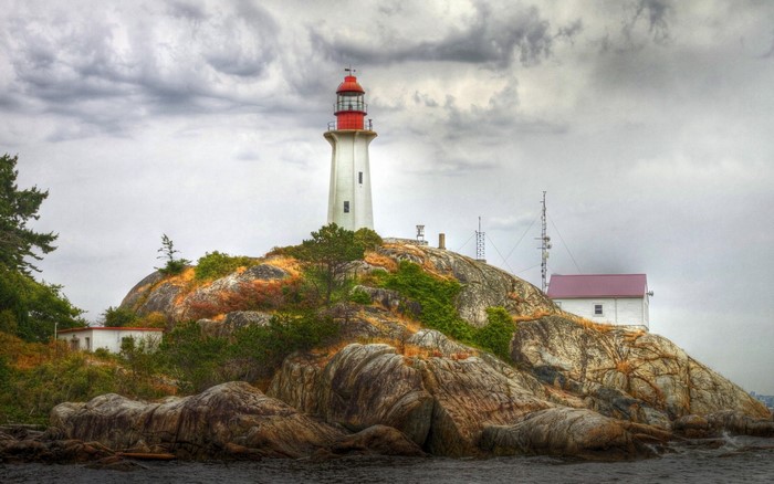 Lighthouse on a rocky island with buildings and antennas