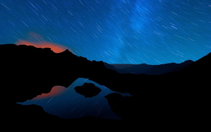 Star trails over mountains and lake at night