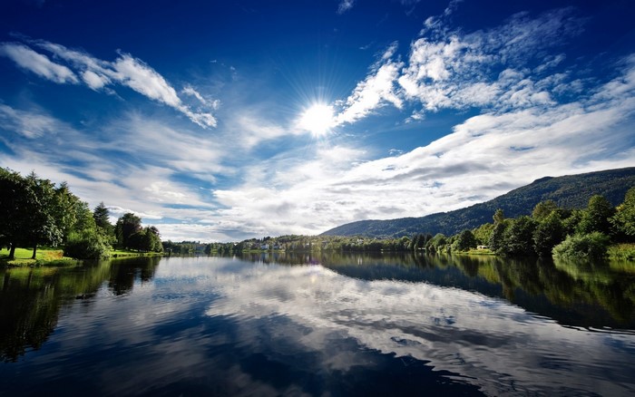 Lake reflection with sun and clouds over mountains