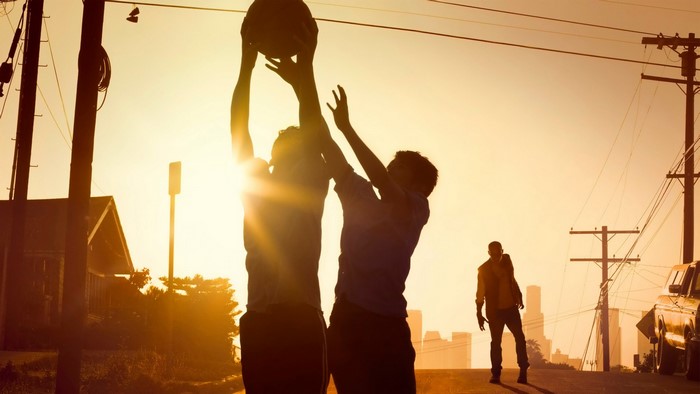 Two people playing basketball at sunset with a third person walking