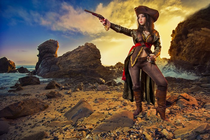 Woman dressed as a pirate holding a pistol on a rocky coast